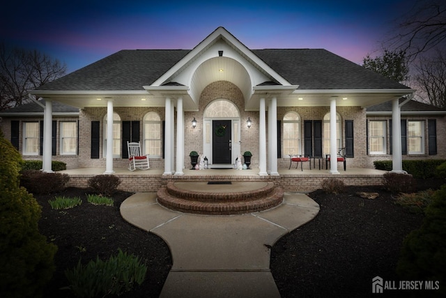 445 Grace Hill Rd, Monroe, NJ 08831 - exterior entry at dusk featuring a shingled roof, covered porch, and brick siding