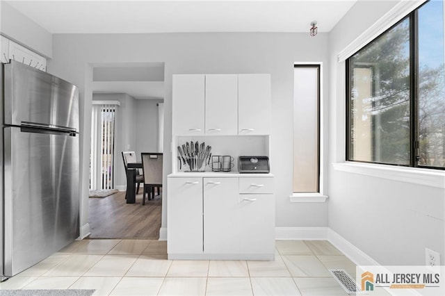 kitchen featuring stainless steel fridge, light tile patterned floors, and white cabinets