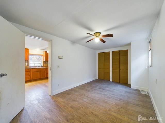 unfurnished bedroom featuring ensuite bathroom, light hardwood / wood-style flooring, and ceiling fan