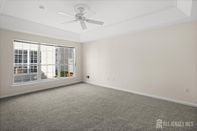 carpeted spare room with a tray ceiling, ceiling fan, and baseboards