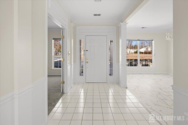 foyer featuring marble finish floor, ornamental molding, decorative columns, and visible vents