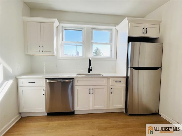 kitchen with white cabinets, light wood-style flooring, stainless steel appliances, and a sink