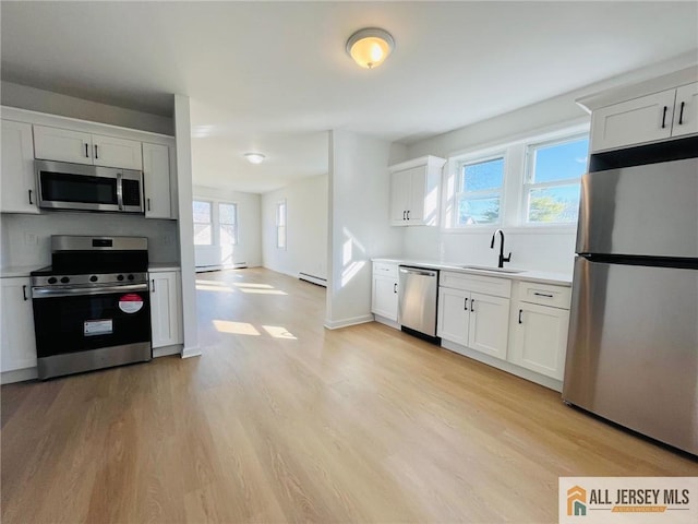 kitchen with light wood-style flooring, stainless steel appliances, a sink, and light countertops