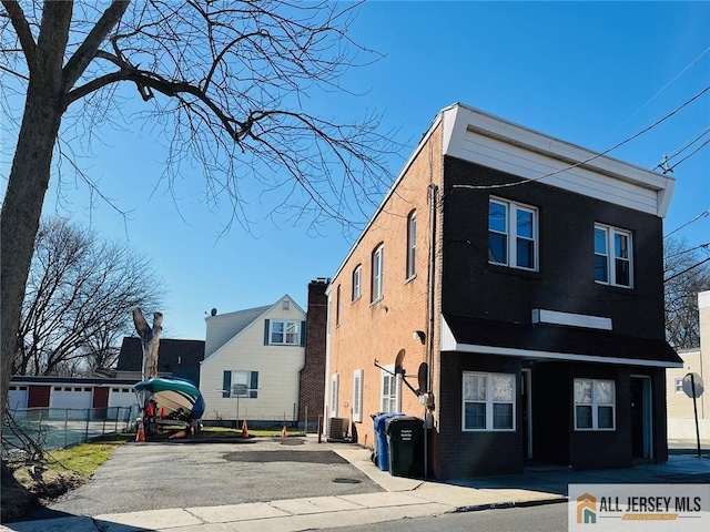 view of front of house featuring brick siding, fence, and central air condition unit