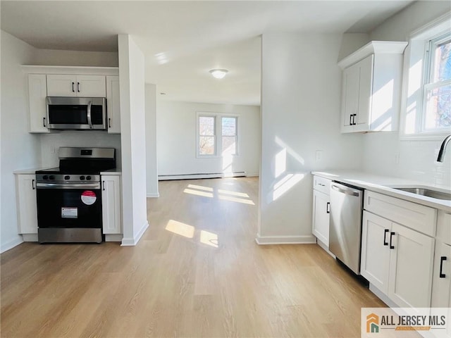 kitchen featuring light wood-type flooring, white cabinets, stainless steel appliances, and a sink