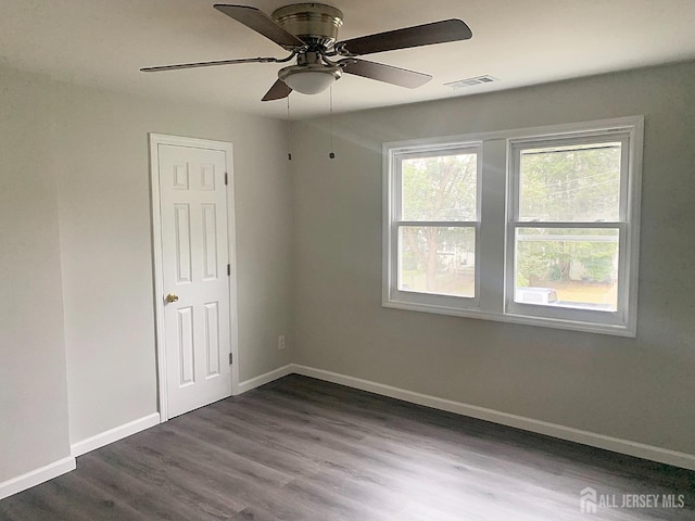 spare room with dark wood-style floors, visible vents, a ceiling fan, and baseboards