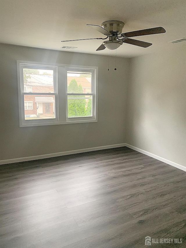 unfurnished room featuring dark wood-style floors, visible vents, a healthy amount of sunlight, and baseboards