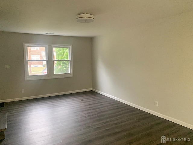 spare room featuring dark wood finished floors, visible vents, and baseboards