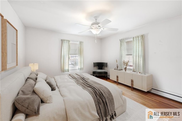 bedroom featuring multiple windows, a baseboard radiator, ceiling fan, and light hardwood / wood-style flooring