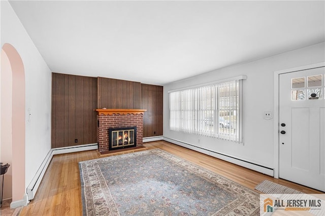 unfurnished living room with a baseboard radiator, wood walls, a fireplace, and light hardwood / wood-style flooring