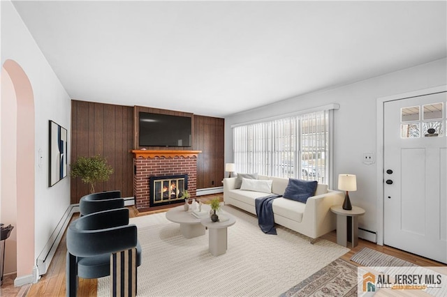 living room with a baseboard radiator, wood walls, a fireplace, and light hardwood / wood-style flooring