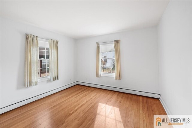 empty room featuring hardwood / wood-style flooring and a baseboard heating unit