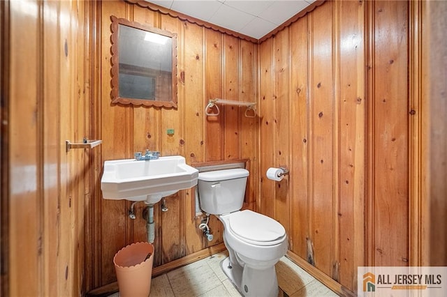 bathroom featuring sink, toilet, and wooden walls