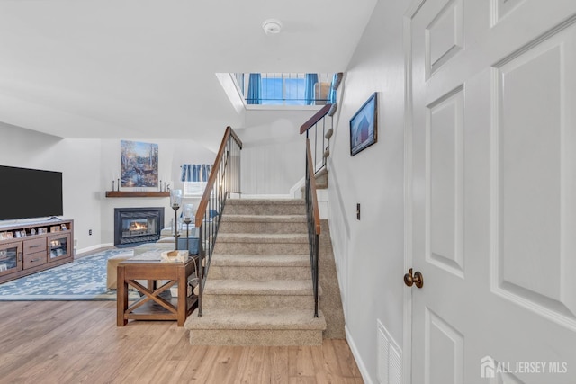 staircase with a skylight, wood finished floors, visible vents, baseboards, and a glass covered fireplace