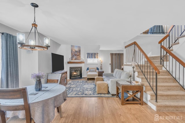 living area with stairs, light wood finished floors, a fireplace with flush hearth, and an inviting chandelier