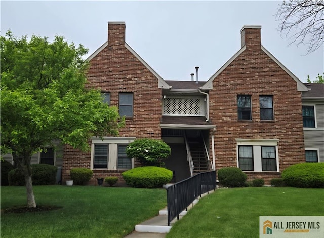 view of front facade featuring brick siding, a chimney, and a front yard
