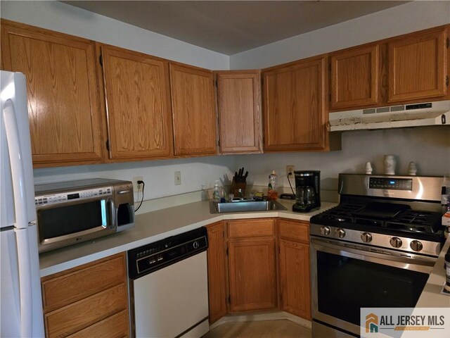 115 Griggs Pl Unit 115, East Brunswick, NJ 08816 - kitchen with under cabinet range hood, stainless steel appliances, light countertops, a sink, and brown cabinetry
