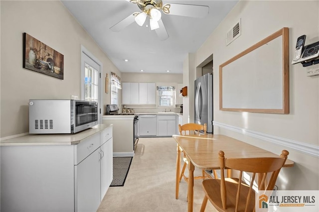 kitchen featuring visible vents, white appliances, white cabinets, light countertops, and ceiling fan