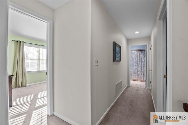 hall featuring visible vents, baseboards, and carpet floors