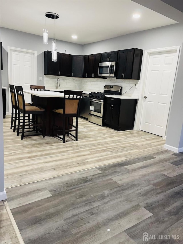 kitchen with light wood-type flooring, backsplash, appliances with stainless steel finishes, a kitchen bar, and pendant lighting