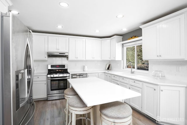 7 Arthurs Ct, Manalapan, NJ 07726 - kitchen featuring appliances with stainless steel finishes, under cabinet range hood, a sink, a breakfast bar area, and wood-type flooring