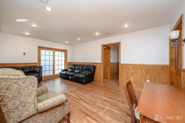 living room with light hardwood / wood-style flooring, wooden walls, and french doors