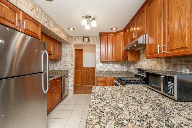 kitchen featuring under cabinet range hood, backsplash, stainless steel appliances, light tile patterned floors, and light stone countertops