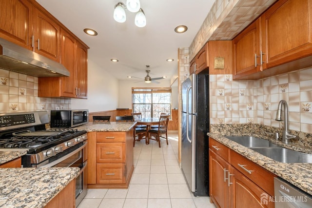 kitchen with brown cabinets, a sink, under cabinet range hood, appliances with stainless steel finishes, and light tile patterned floors