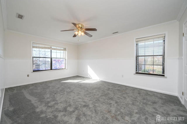 empty room with a wainscoted wall, visible vents, dark carpet, crown molding, and ceiling fan