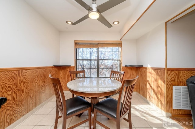 dining space featuring light tile patterned floors, visible vents, wood walls, and wainscoting