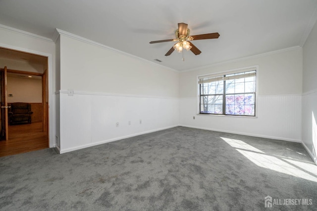 carpeted empty room featuring ceiling fan, a wainscoted wall, and ornamental molding