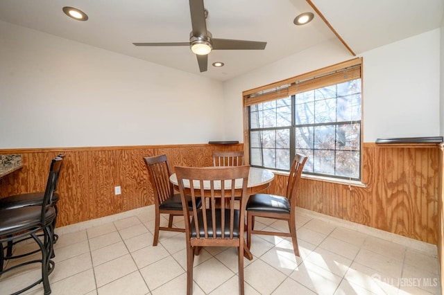 dining space featuring light tile patterned floors, ceiling fan, and wood walls