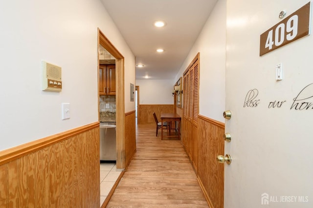 corridor featuring recessed lighting, a wainscoted wall, light wood-style floors, and wooden walls