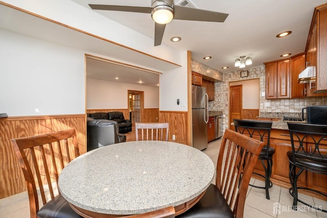 dining space featuring light tile patterned floors, ceiling fan, and wood walls