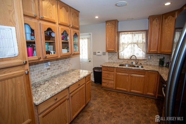 kitchen with brown cabinetry, stainless steel fridge, light stone countertops, and a sink