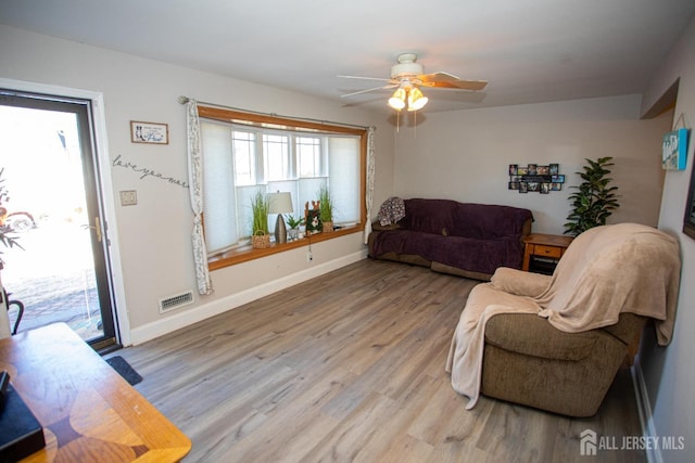 living area with visible vents, baseboards, light wood-style floors, and a ceiling fan