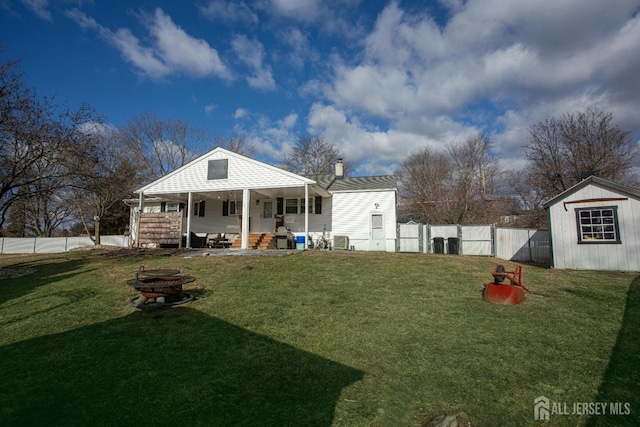 back of property featuring fence, a chimney, an outdoor structure, a fire pit, and a lawn