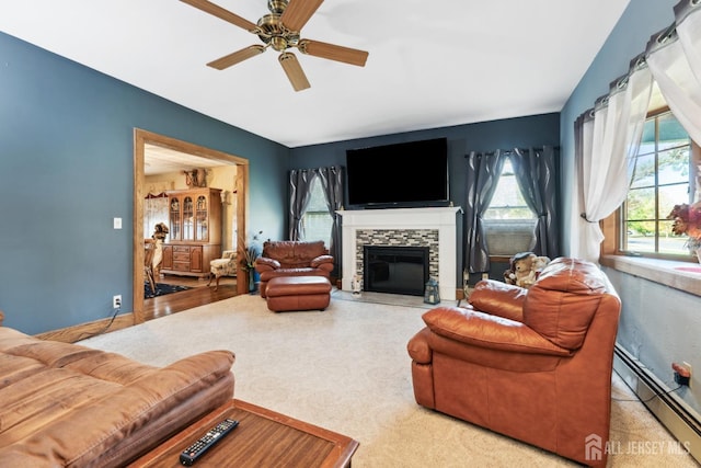 living room featuring ceiling fan, baseboard heating, light carpet, and a stone fireplace