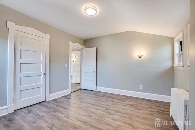 unfurnished room featuring light wood-style floors, lofted ceiling, radiator, and baseboards