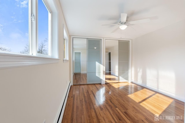 unfurnished bedroom with a baseboard radiator, baseboards, and wood finished floors