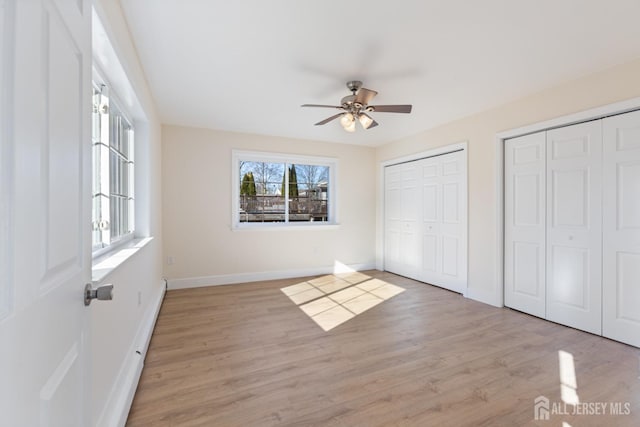 unfurnished bedroom featuring light wood-type flooring, multiple closets, baseboards, and a ceiling fan