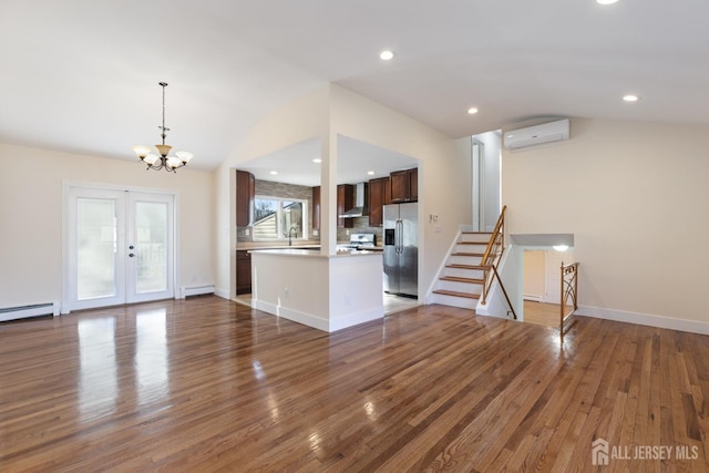 unfurnished living room with a baseboard heating unit, vaulted ceiling, wood finished floors, and a wall mounted air conditioner