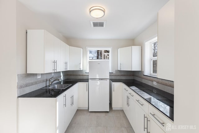 kitchen featuring visible vents, a sink, dark countertops, white cabinetry, and freestanding refrigerator