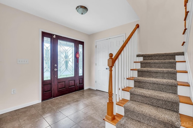 tiled foyer featuring baseboards and stairs