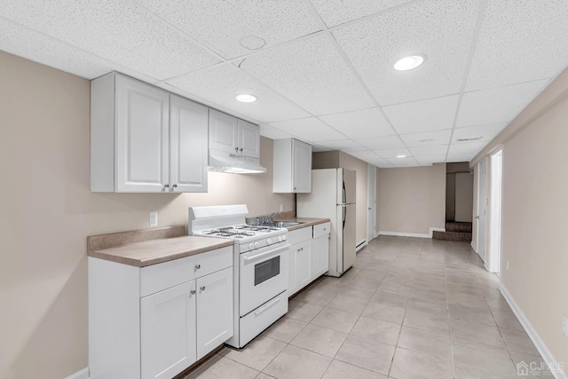 kitchen featuring white appliances, light countertops, under cabinet range hood, and baseboards