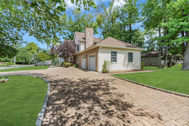 view of property exterior with an attached garage, brick siding, decorative driveway, a lawn, and a chimney