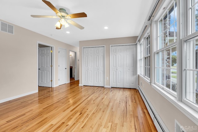 unfurnished bedroom with a baseboard heating unit, baseboards, visible vents, and multiple closets