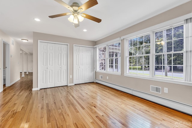 unfurnished bedroom with a baseboard radiator, recessed lighting, baseboards, light wood finished floors, and two closets