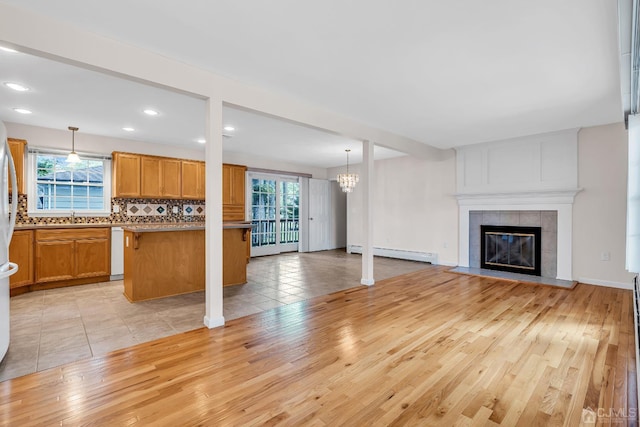 unfurnished living room with light wood finished floors, a tiled fireplace, a baseboard radiator, a sink, and recessed lighting