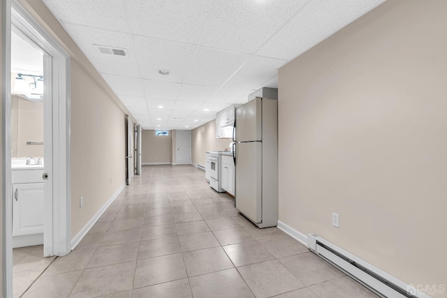 corridor featuring a baseboard radiator, visible vents, a sink, a drop ceiling, and baseboards